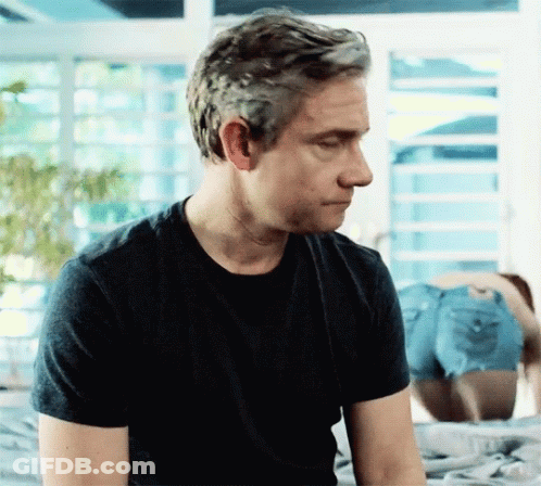 A Man In A Black T-Shirt Is Sitting On A Bed With His Eyes Closed GIF