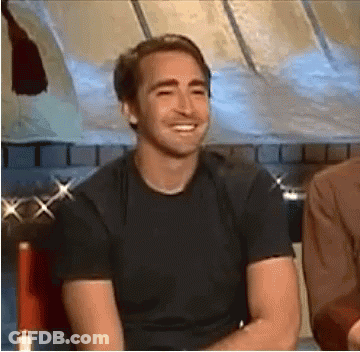 A Man In A Black T-Shirt Is Smiling While Sitting In A Chair . GIF