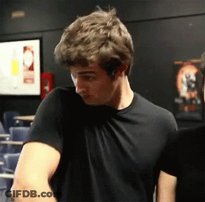 A Man In A Black T-Shirt Is Standing In A Dark Room . GIF