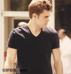 A Man In A Black T-Shirt Is Standing In Front Of A Door GIF