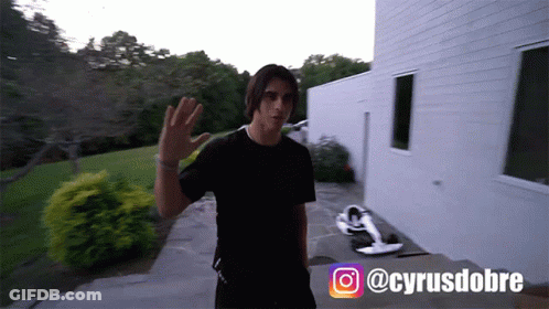 A Man In A Black T-Shirt Is Standing In Front Of A White Building With The Hashtag @Cyrusdobre On The Bottom GIF