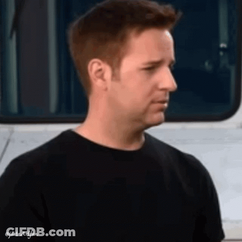 A Man In A Black T-Shirt Is Standing In Front Of A White Van . GIF