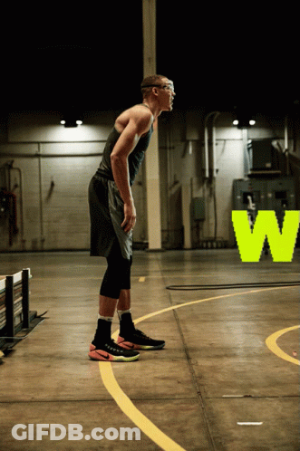 A Man In A Black Tank Top And Black Shorts Stands On A Basketball Court In Front Of A Neon W Sign GIF