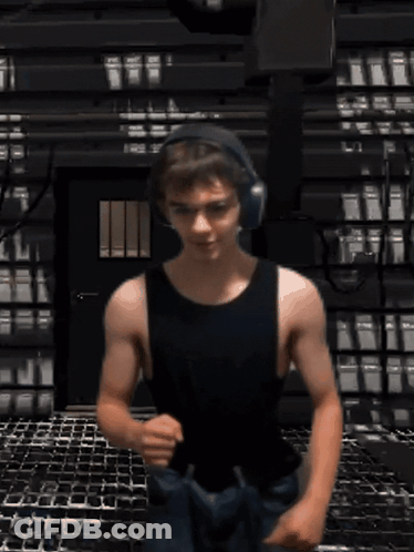 A Man In A Black Tank Top And Headphones Is Running GIF