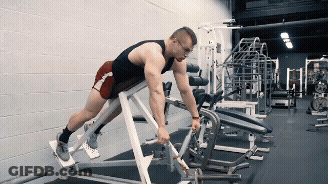 A Man In A Black Tank Top And Red Shorts Is Using A Machine In A Gym GIF