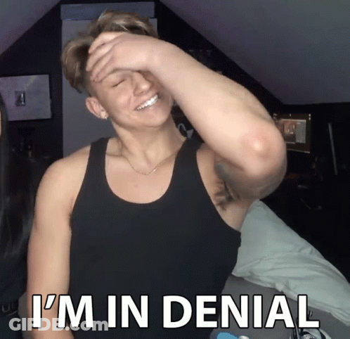 A Man In A Black Tank Top Covering His Face With His Hand And The Words I 'M In Denial Below Him GIF