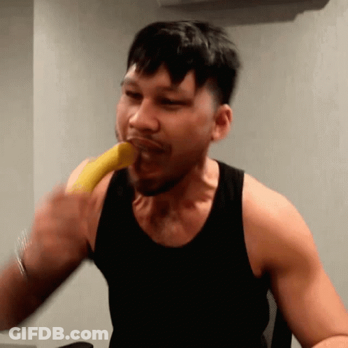A Man In A Black Tank Top Is Biting A Banana GIF
