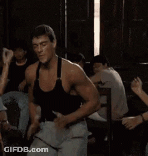 A Man In A Black Tank Top Is Dancing In A Room With Other People GIF
