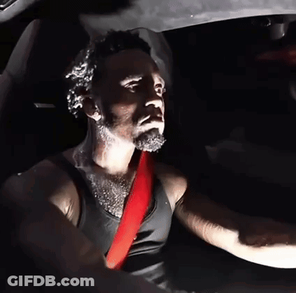 A Man In A Black Tank Top Is Driving A Car With A Red Seat Belt GIF
