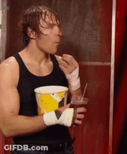 A Man In A Black Tank Top Is Holding A Cup Of Popcorn And A Drink . GIF