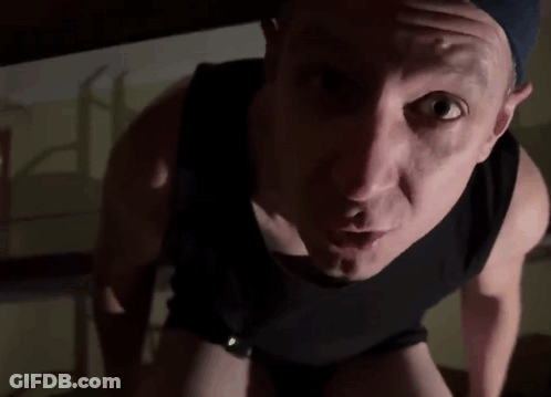 A Man In A Black Tank Top Is Looking At The Camera With His Mouth Open . GIF