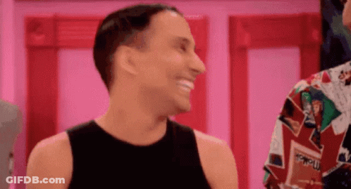 A Man In A Black Tank Top Is Smiling And Laughing While Standing Next To Another Man In A Colorful Shirt . GIF