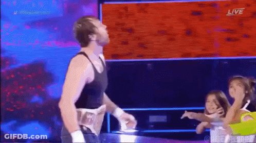 A Man In A Black Tank Top Is Standing In A Wrestling Ring With A Group Of Children . GIF