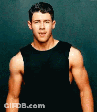 A Man In A Black Tank Top Is Standing In Front Of A Black Wall . GIF