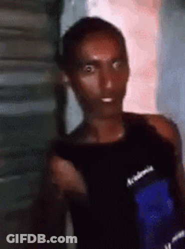 A Man In A Black Tank Top Is Standing In Front Of A Building . GIF