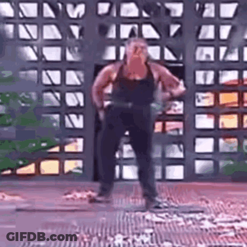 A Man In A Black Tank Top Is Standing In Front Of A Fence . GIF