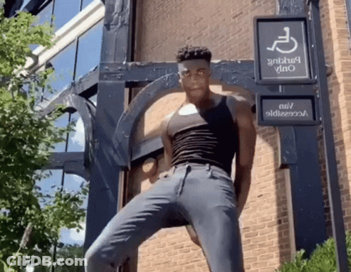 A Man In A Black Tank Top Is Standing In Front Of A Handicap Sign GIF
