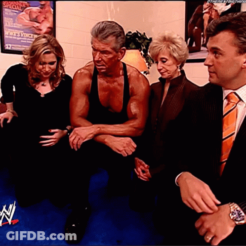 A Man In A Black Tank Top Sits Between Two Women And A Man In An Orange Tie GIF