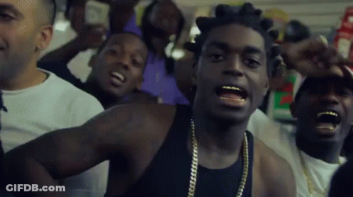 A Man In A Black Tank Top With Gold Chains Around His Neck Is Surrounded By Other Men GIF