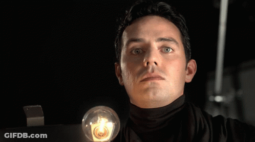 A Man In A Black Turtleneck Is Holding A Light Bulb In Front Of The Word Thats GIF