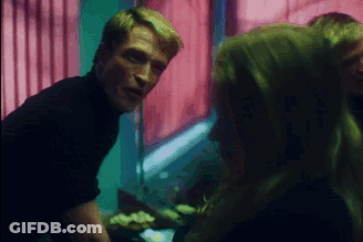A Man In A Black Turtleneck Talks To A Woman In A Dark Room GIF