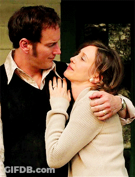 A Man In A Black Vest Is Hugging A Woman In A White Sweater GIF