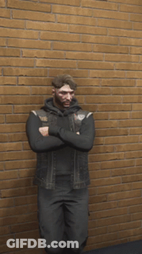 A Man In A Black Vest Is Standing In Front Of A Brick Wall GIF