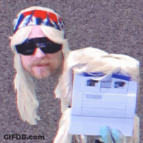 A Man In A Blonde Wig And Sunglasses Holds A Printer GIF