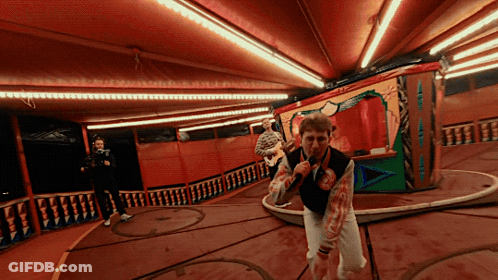 A Man In A Bloody Vest Is Holding A Microphone In A Room GIF