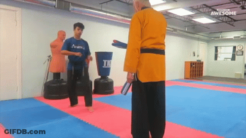 A Man In A Blue Academy Shirt Is Kicking A Man In A Yellow Robe GIF
