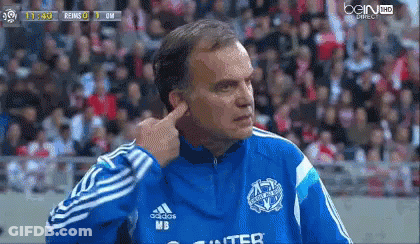 A Man In A Blue Adidas Jacket Is Covering His Ears During A Soccer Game GIF