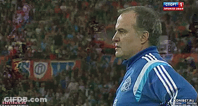 A Man In A Blue Adidas Shirt Stands In Front Of A Sign That Says Soft GIF