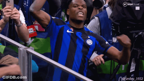 A Man In A Blue And Black Striped Shirt Stands In Front Of A Bt Sport 1 Live Camera GIF