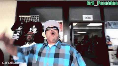 A Man In A Blue And Gray Plaid Shirt Stands In Front Of A Store With A Sign That Says 1008 GIF