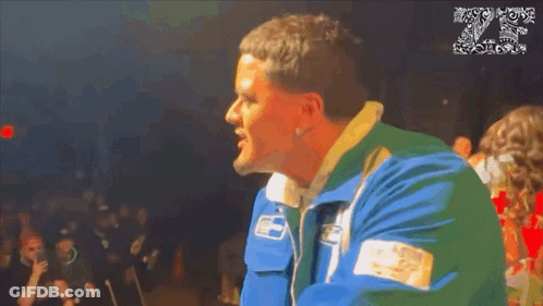A Man In A Blue And Green Jacket Stands In Front Of A Crowd With The Number 20 On The Bottom GIF