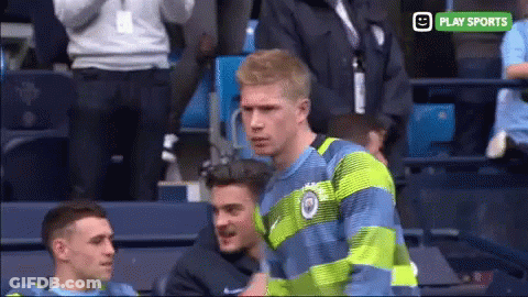 A Man In A Blue And Green Striped Shirt Stands In A Stadium With A Play Sports Logo Behind Him GIF