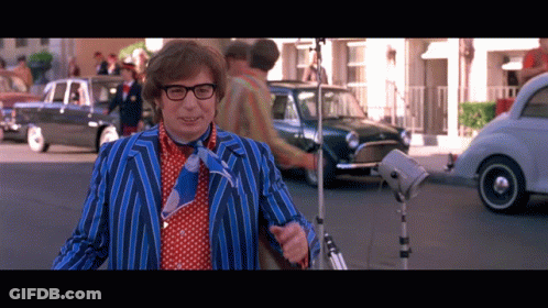 A Man In A Blue And Red Striped Suit And Tie Stands On A Street GIF