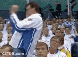 A Man In A Blue And White Jacket Is Standing In Front Of A Crowd Of People GIF