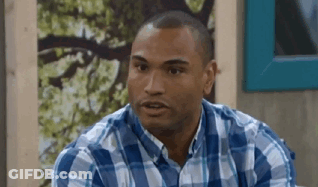 A Man In A Blue And White Plaid Shirt Is Sitting In Front Of A Wall . GIF