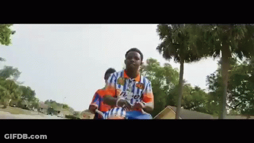A Man In A Blue And White Shirt Is Riding A Bicycle On A Street . GIF