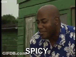 A Man In A Blue And White Shirt Says Spicy In Front Of A Green Building . GIF