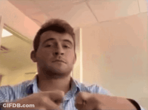 A Man In A Blue And White Striped Shirt Is Making A Funny Face While Holding His Hands Together . GIF
