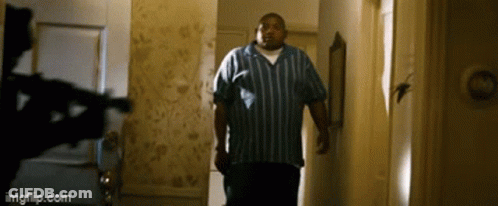 A Man In A Blue And White Striped Shirt Is Walking Down A Hallway . GIF