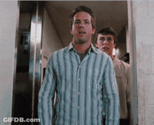 A Man In A Blue And White Striped Shirt Stands In A Doorway GIF