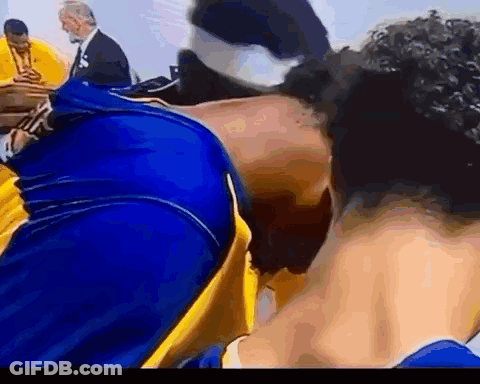 A Man In A Blue And Yellow Shirt Is Kissing Another Man On The Cheek . GIF