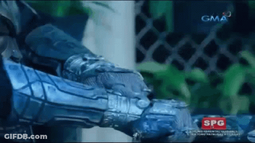 A Man In A Blue Armor Is Standing In Front Of A Fence And A Gma Logo . GIF