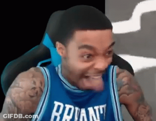 A Man In A Blue Basketball Jersey Is Sitting In A Chair With His Tongue Hanging Out . GIF