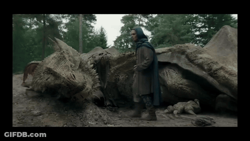 A Man In A Blue Cape Stands Next To A Dead Dragon In The Dirt GIF