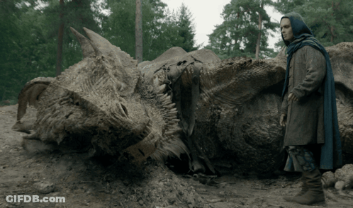 A Man In A Blue Cape Stands Next To A Large Dragon Skeleton GIF