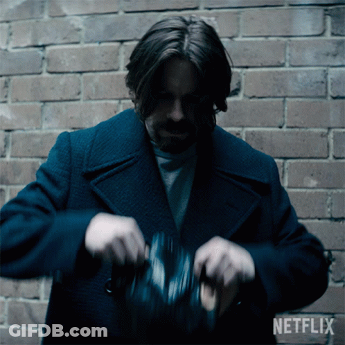 A Man In A Blue Coat Is Standing In Front Of A Brick Wall With A Netflix Logo Behind Him GIF